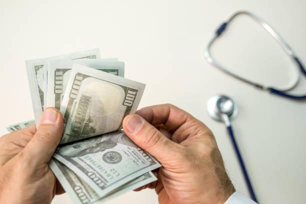 istock Doctor's Hand Counting Banknotes, The Relationship Between Money and Health 2191942046