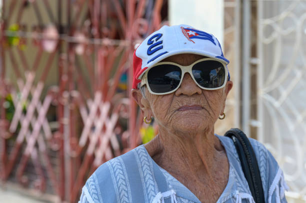 Santa Clara, Cuba - December 23, 2024: Portrait of senior Cuban woman wearing a baseball cap with the Cuban flag. Candid street portrait.