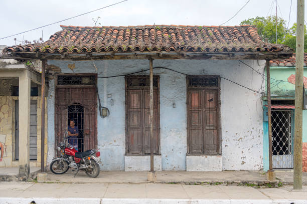 Santa Clara, Cuba - December 20, 2024: A Cuban man stands in the door of a colonial house with a weathered facade and a tile roof.