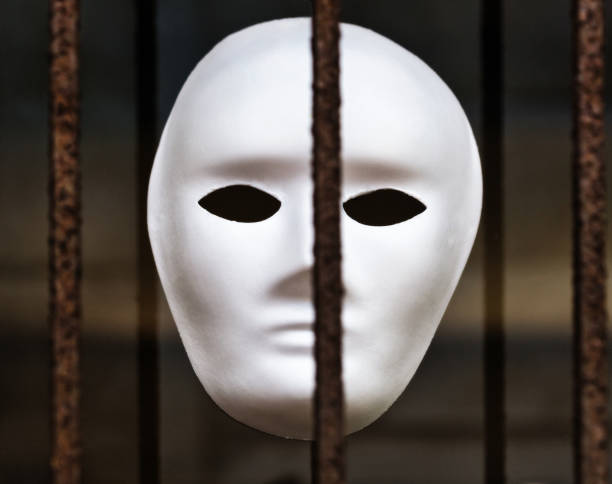 Representing entrapment or captivity, a white paper face mask stares out from behind rusty iron bars.