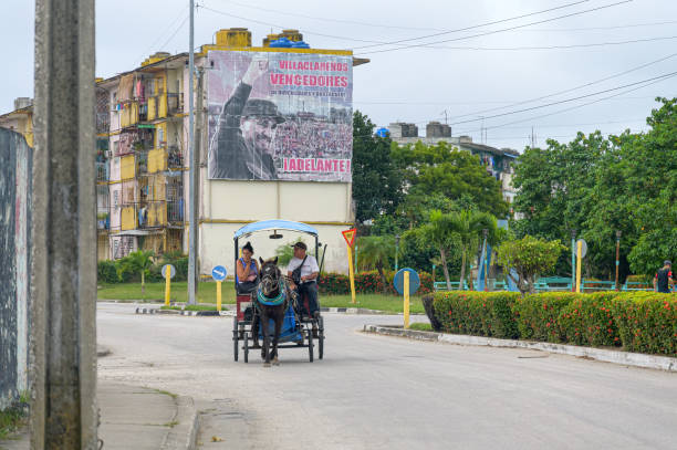 One of Cuba's old cars rides in front of a sign featuring revolutionary Cuban leaders.