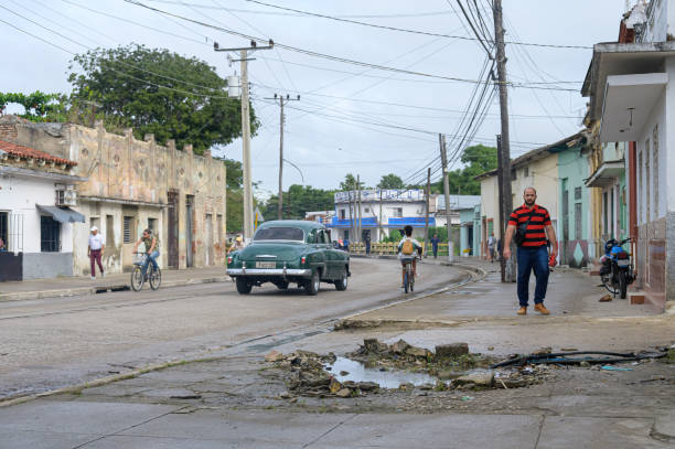 Santa Clara, Cuba - December 20, 2024: A leak of water in the broken sidewalk. Cuban people are out and about in the area.