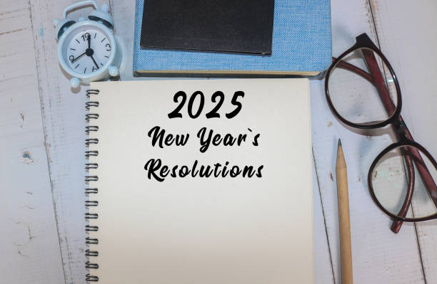 istock A workspace featuring a notepad with 2025 New Year's resolutions, glasses, a pen, books, and clock 2191954428