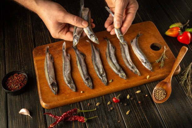 istock Hands skillfully arrange freshly caught fish on a wooden board, surrounded by vibrant herbs and spices. The kitchen exudes warmth, promising delicious flavors ahead 2191959358
