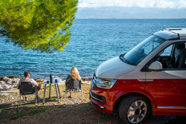 istock Red Camper Van Parked While Couple Enjoys Seaside Coffee Break 2191960750