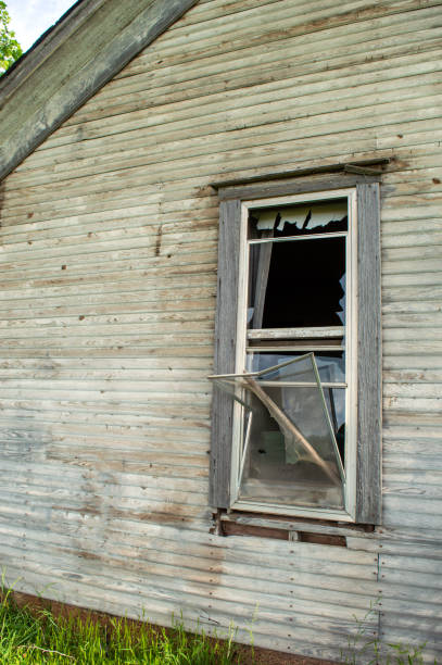 Raw bare exterior farm halls walls with a broken window shows this old house has been abandoned for many years.