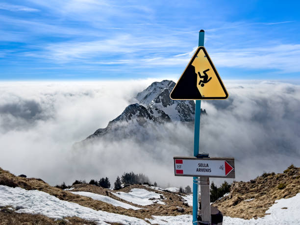 Danger of falling sign placed at the edge of a cliff side and mountain surrounded in clouds in Zoncolan