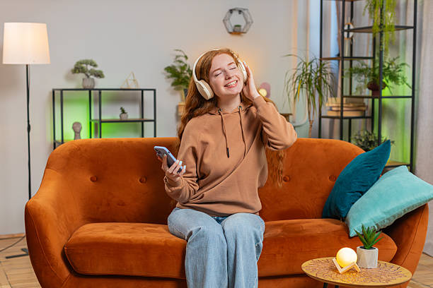 istock Happy overjoyed young woman in wireless headphones using smartphone relaxing sitting on sofa at home 2191978172