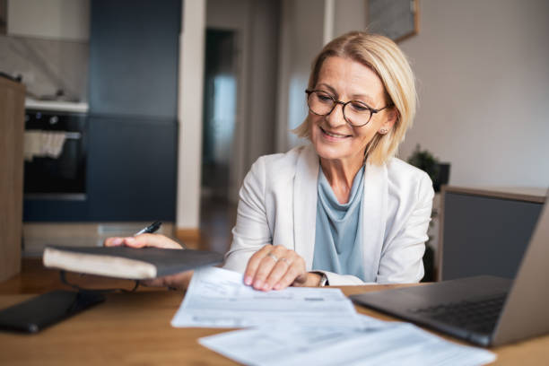istock Senior woman working from home reviewing documents at desk 2191978244