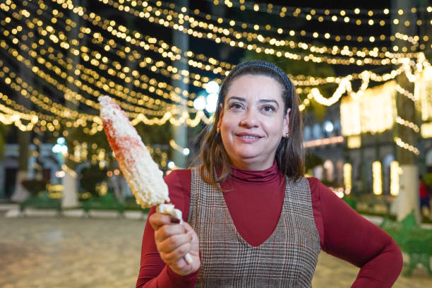 Mexican woman holding corn on the cob at night market with christmas lights
