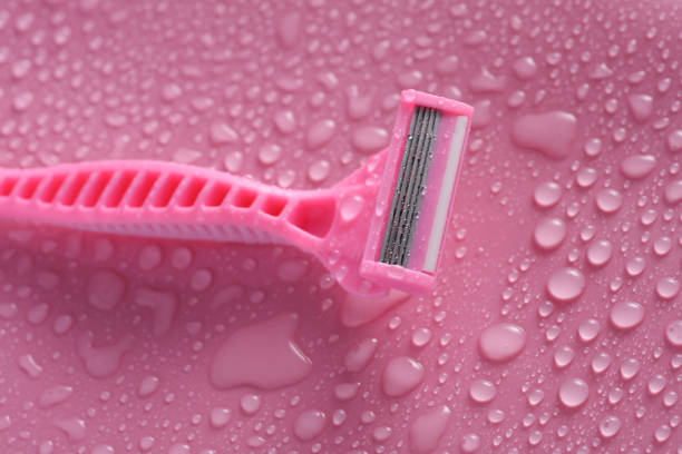 Plastic disposable razor on a pink background with water drops