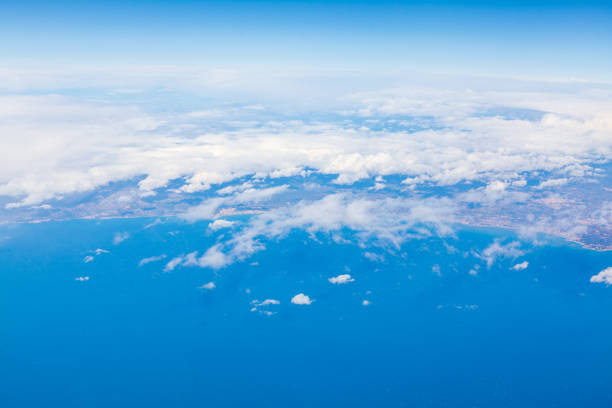 Aerial view of the ocean and fluffy clouds, showcasing the vast blue expanse from an airplane window. Overhead perspective of sea and clouds, captured from an airplane, highlighting nature's beauty