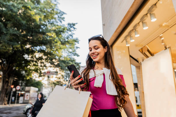 istock Young woman using the mobile phone while walking in the street 2192012051