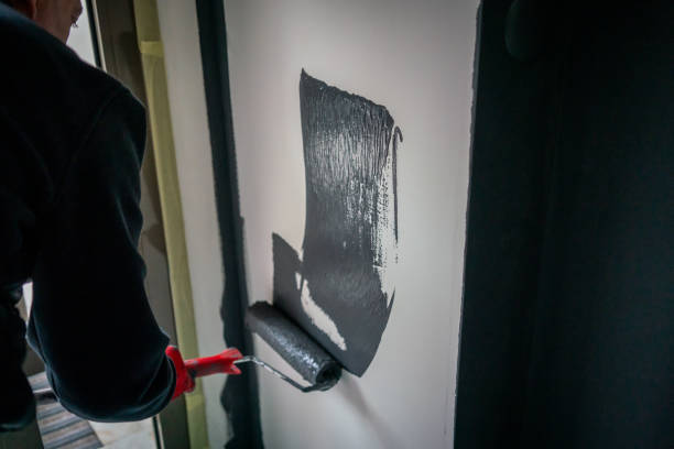 paint roller is in male painter hand on wall he is painting horizontal fixer upper home still