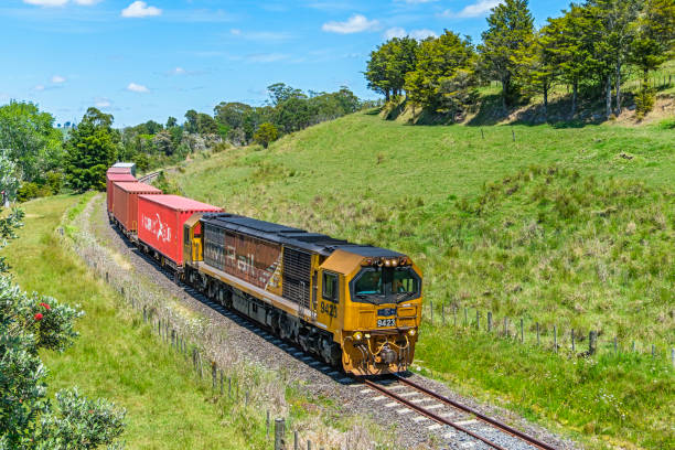 Whangarei, New Zealand - Dec 03, 2024: A short KiwiRail container freight train approaches the State Highway 1 overpass at Oakleigh as it nears its destination at Whangerei in Northland, having travelled from Auckland. The narrow gauge (3'6\