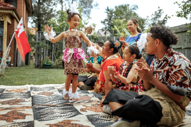 Pacific Islanders family sitting on carpet while wearing traditional clothes, little girl is dancing