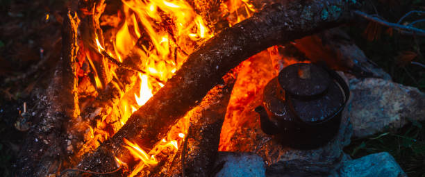 istock Boiling of tea in kettle on bonfire with large firewood. Tea drinking in open air. Active outdoor recreation. Camping in dusk. Romantic warm atmosphere in twilight on nature. Active rest. 2192027108