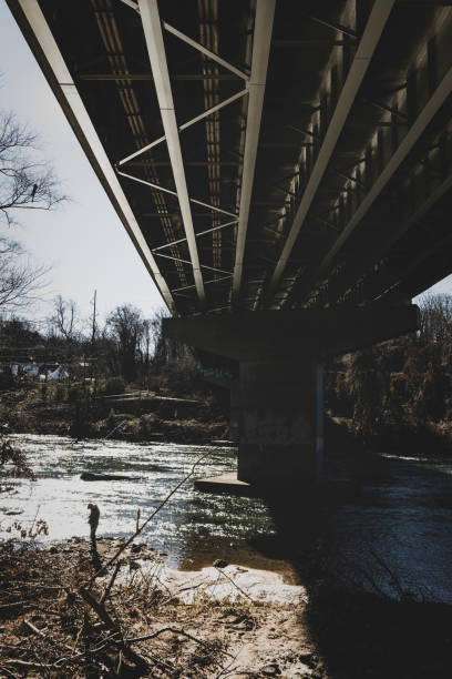 A man stands beside the French Broad River and under the Riverlink Bridge in Asheville, North Carolina, about two months after the record-breaking flood (December 6, 2024)