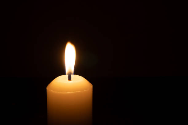 istock A single burning candle flame or light glowing on a big white candle isolated on red or dark background on table in church for Christmas, funeral or memorial service 2192035490