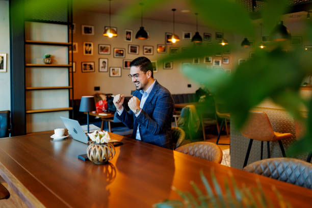 istock Businessman celebrating success while working on laptop in cafe 2192037574