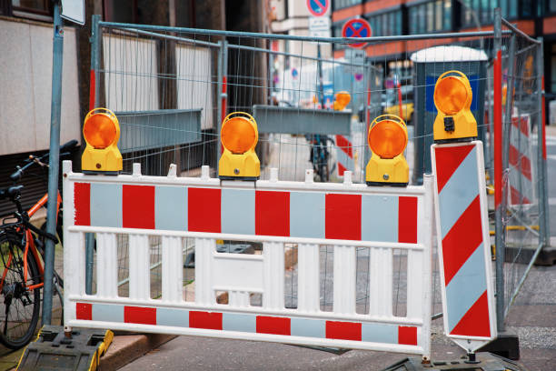 Red and white striped construction barriers with flashing yellow lights blocking access to a city street