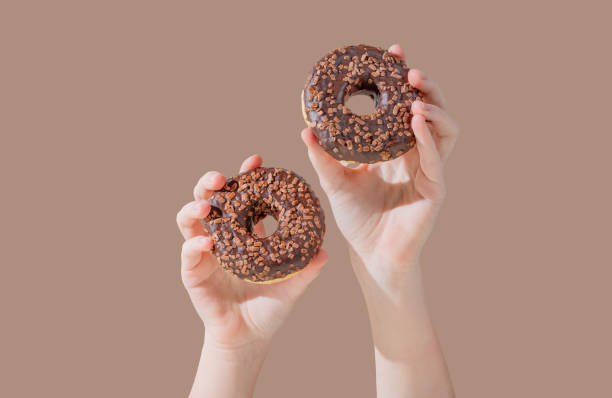 istock Hands holding two glazed chocolate donuts on mocha brown background. 2192049141