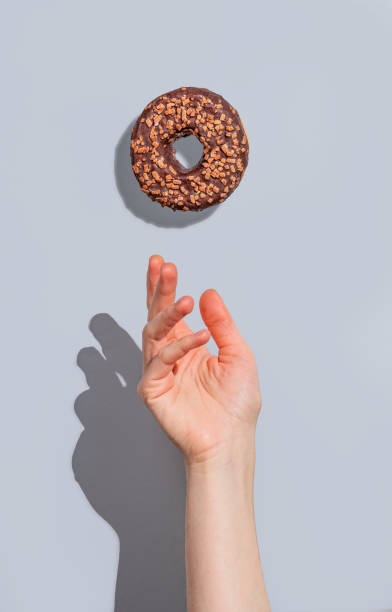istock Hand with flying glazed chocolate donut on blue background with shadow. 2192049716