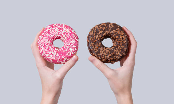 istock Hands holding two glazed chocolate and pink donuts on blue background. 2192050258