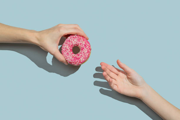 istock Hand holding glazed pink donut to other hand on blue background. 2192050397