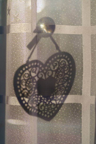 A captivating photograph showcasing a beautifully intricate heart-shaped ornament casting an elegant shadow on a sheer curtain. The delicate lace details of the heart are highlighted against the soft, diffused light. Perfect for adding a touch of romance and elegance to any project.