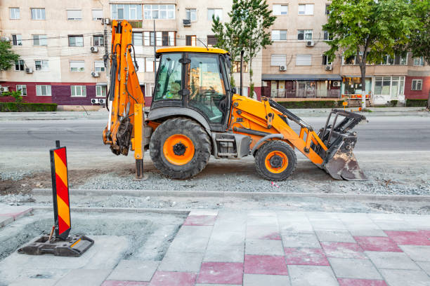 A yellow tractor with front and rear hydraulic buckets stands on a construction site in the city.