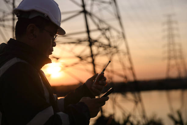 High voltage engineer with safety PPE  suit hold drawing blueprint under electric power poles at sunset