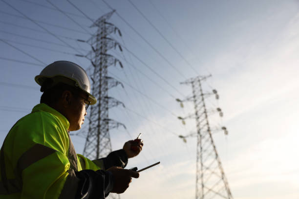 istock Senior high voltage engineer with green safety jacket and hardhat working on laptop and walkie talkie at the power plant under the electrical pole 2192057983