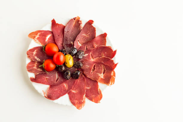 A plate features thinly sliced beef carpaccio arranged with brown bread slices and a drizzle of olive oil. Capers add a touch of flavor to the dish.