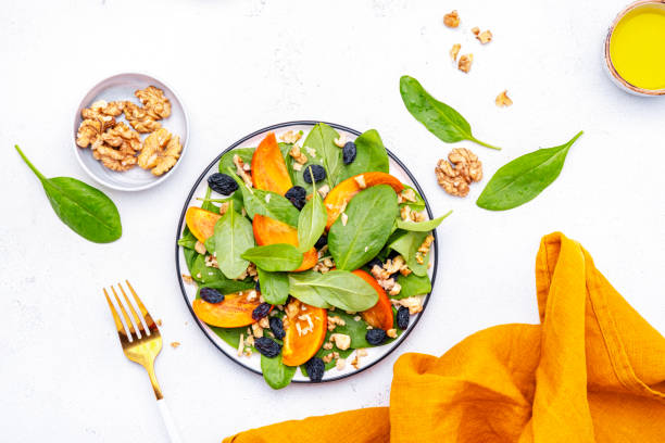 istock Wintervegan persimmon salad with walnuts, blue raisin and spinach, white background, top view 2192080002