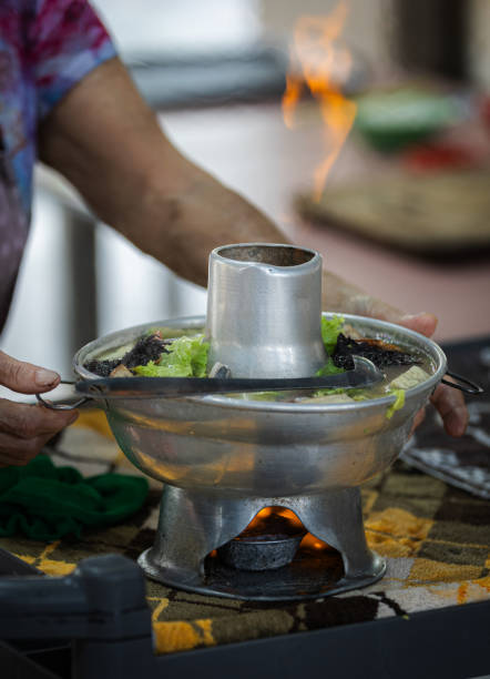 Old woman is serving hot tom yum soup in hawker center.Asian street food, Singapore city.