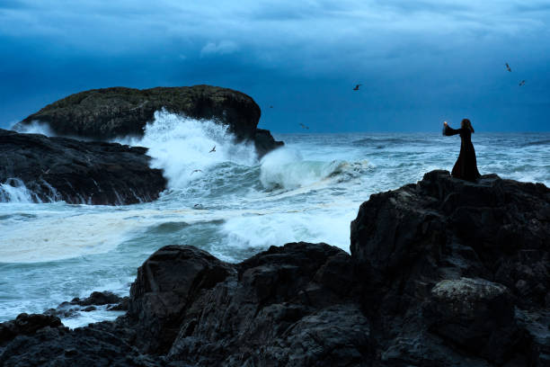Woman stands on rocks during high tide on a western coast  beach, Tofino, Vancouver Island, British Columbia, Canada