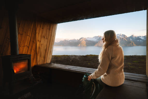 istock Woman is warming herself by the fireplace in a mountain hut with panoramic window in Norway, travel lifestyle autumn vacations backpacking trip, hiker girl in a cozy house alone 2192101152