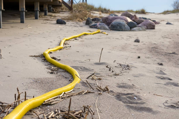 A long and yellow plastic tube bends between rocks on the beach