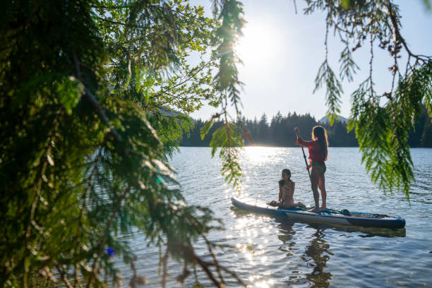 Mother and daughter enjoy SUP board on mountain lake, view through tree branches , Whistler, B.C.