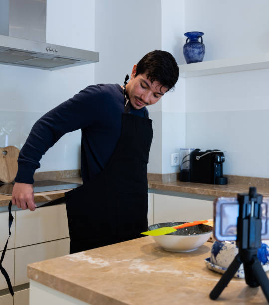 istock Vertical image of a young man putting on an apron to make a tutorial with his cell phone on how to cook a dessert at home 2192115779