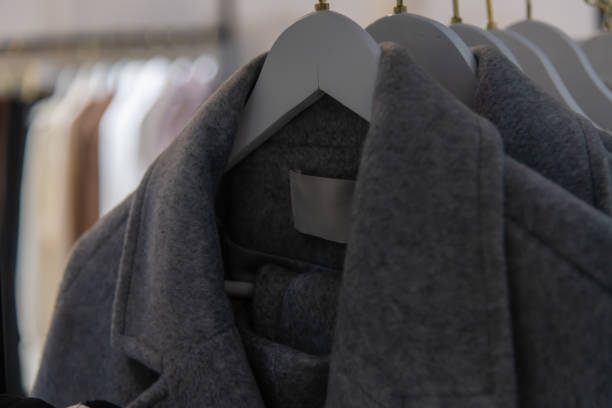 Close-up view of dark gray wool coats with blank labels hanging on hangers in clothing store. Soft focus. Copy space. Autumn and winter warm clothes. Fashion and retail business theme.