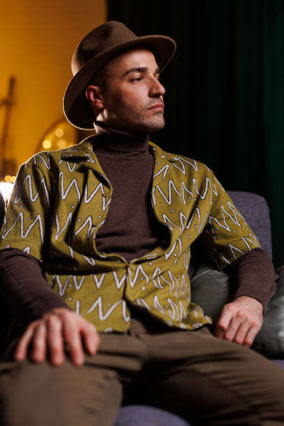 istock Stylish man in hat and patterned shirt sitting creatively in vibrant lighting 2192125037