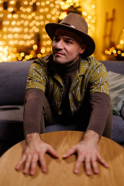 istock Man sitting casually on a sofa with stylish hat and cozy ambiance background 2192125050