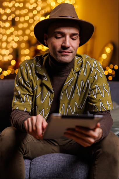 istock Man in a hat using a tablet indoors with warm bokeh light background 2192125088