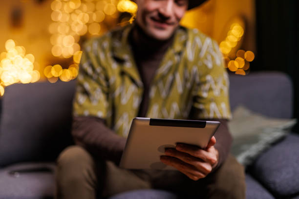 Man holding a tablet while seated in a cozy living room ambiance