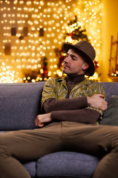 istock Man sitting on a sofa with festive lights and holiday decorations in background 2192125112