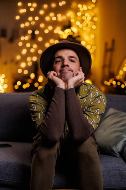 istock Thoughtful young man sitting on a cozy couch with festive lights ambient glow 2192125154