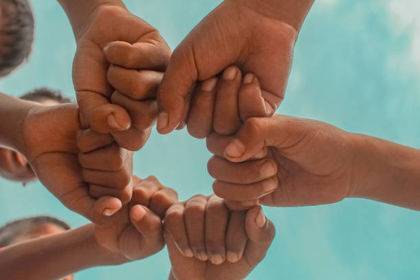 istock Below, boys' hands, collaboration, partnership, and grouping against a sky background. Low angle, peace and friends signs support teamwork, goals, and missions. 2192128016