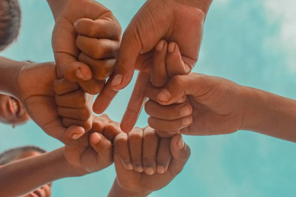 istock Below, boys' hands, collaboration, partnership, and grouping against a sky background. Low angle, peace and friends signs support teamwork, goals, and missions. 2192128017